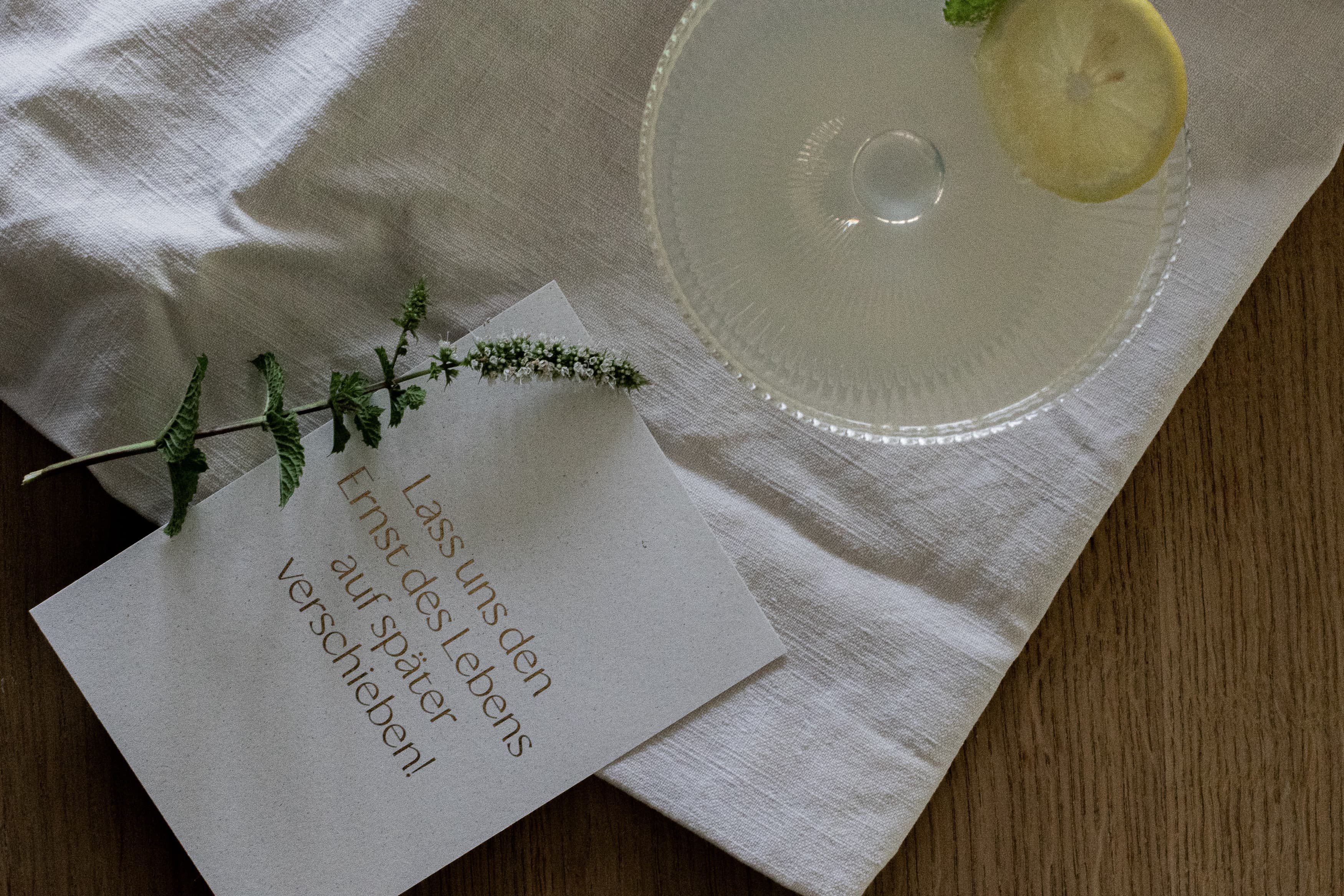 Karte liegt mit Cocktailglas auf Tisch – Lass uns den Ernst des Lebens verschieben | Studio Wiis